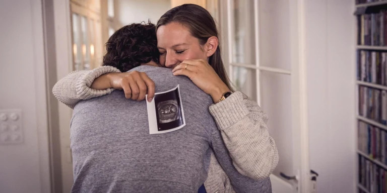  Frau mit Ultraschall-Bild in der Hand umarmt Mann