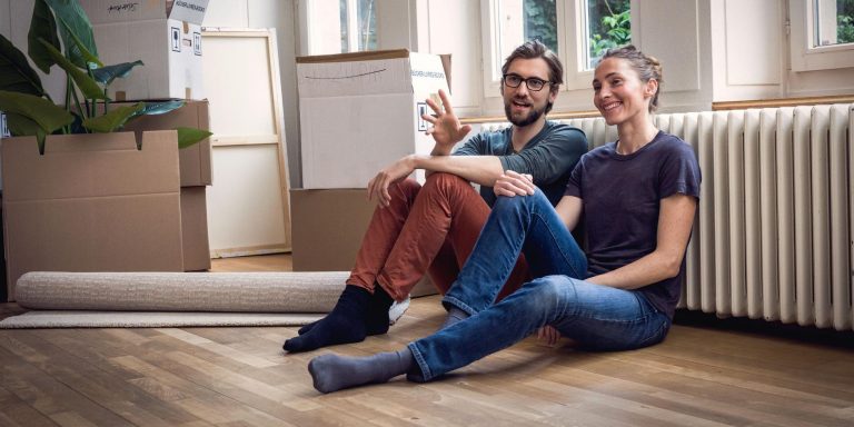 Young couple sitting in an unfurnished flat, surrounded by moving boxes