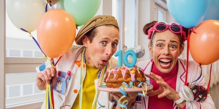 Two Giggle Doctors holding a Gugelhupf cake, which has the number 10 on it