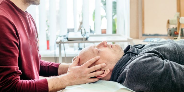 standing person places their hands on the side of the head of a person lying on their back